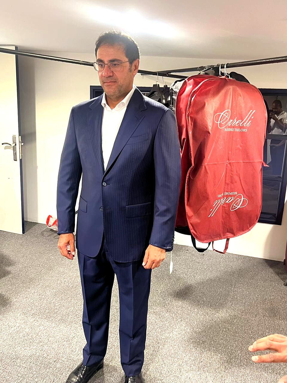 Client in a finished navy chalk-stripe suit beside a Carelli Bespoke garment bag