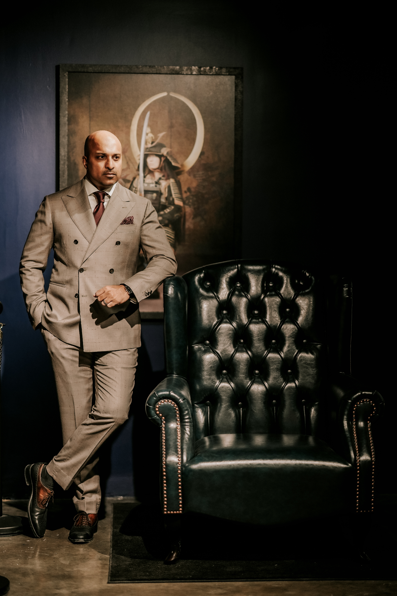 Client in a stone glen-check double-breasted suit beside a green leather chair