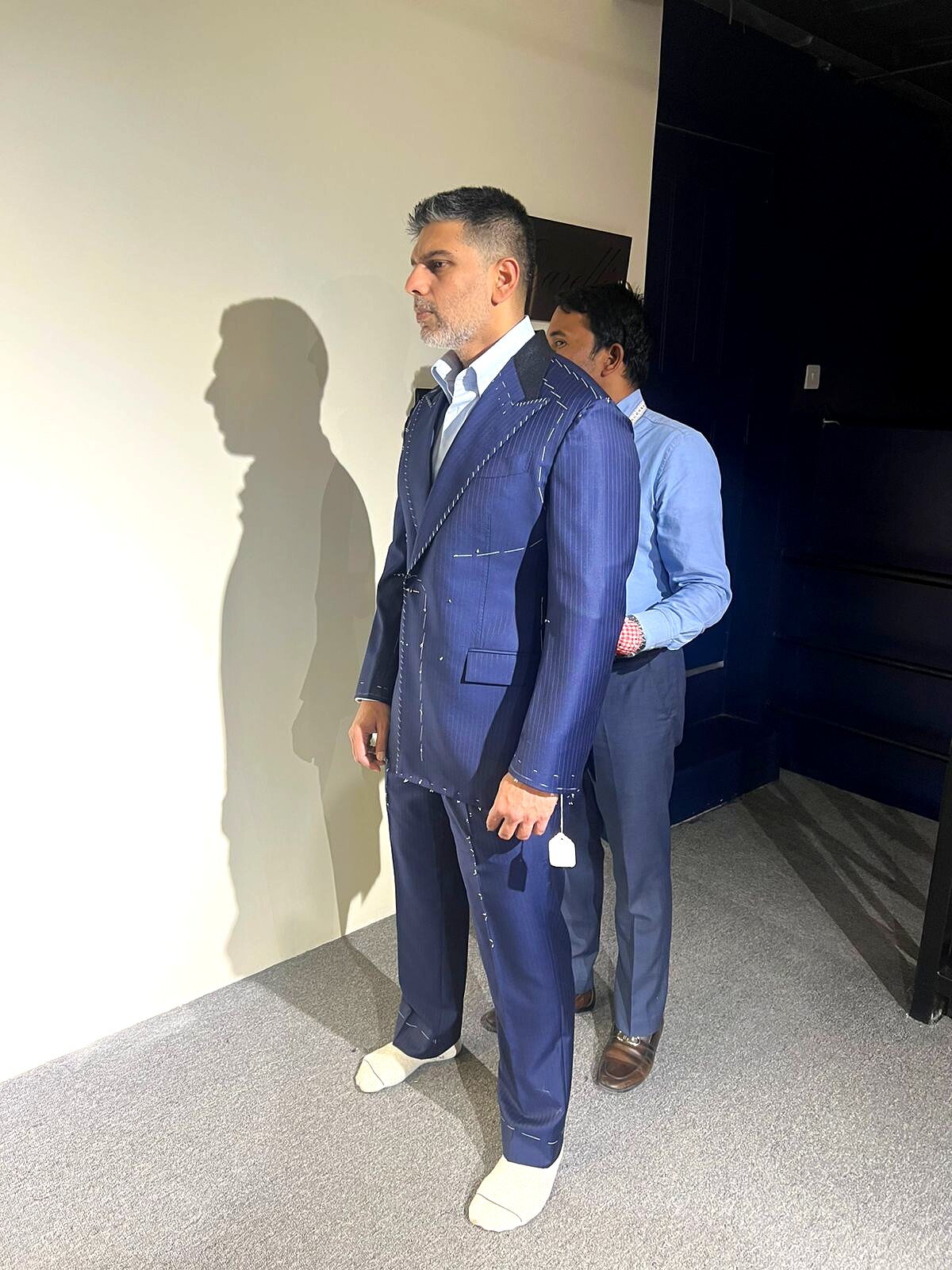 Client in a basted navy pinstripe suit during a forward fitting at the atelier