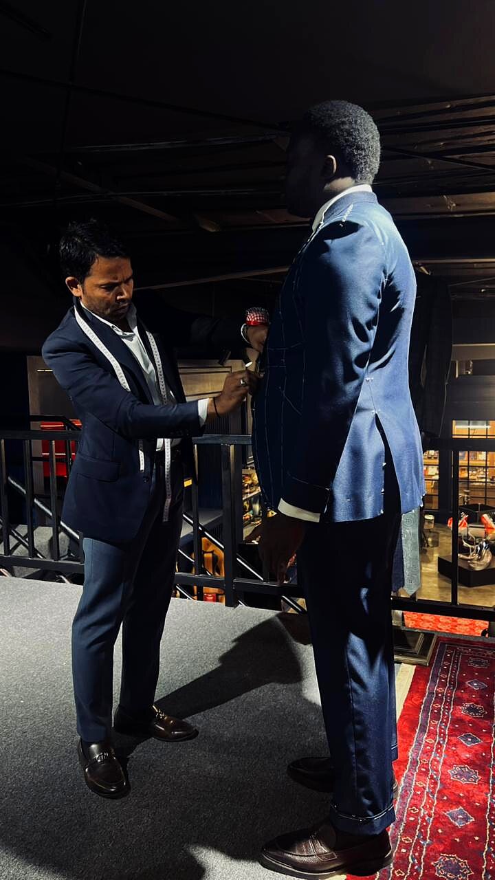 Tailor adjusting a navy basted jacket from the side on a tall client