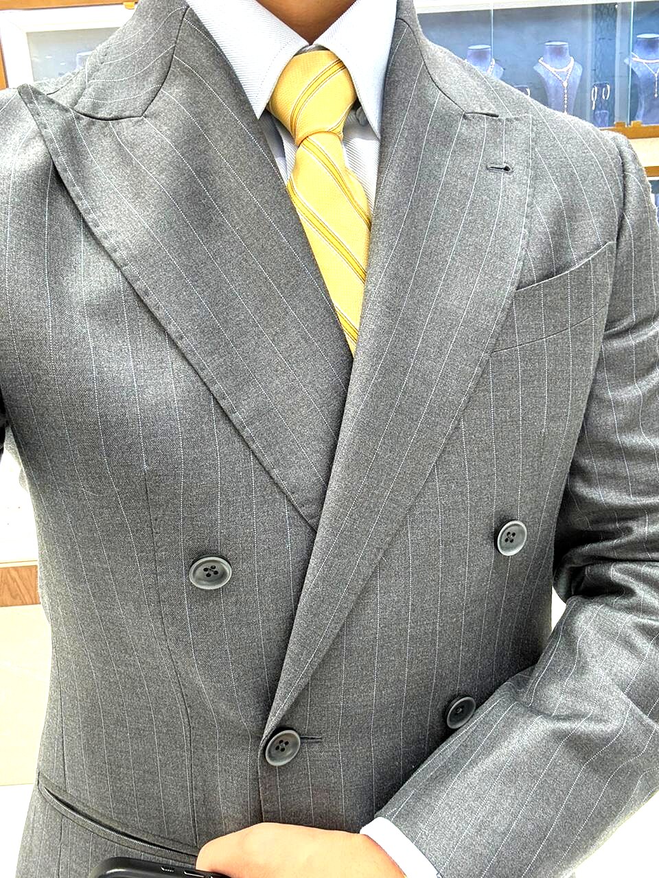 Close-up of a grey pinstripe double-breasted jacket with peak lapels and yellow striped tie