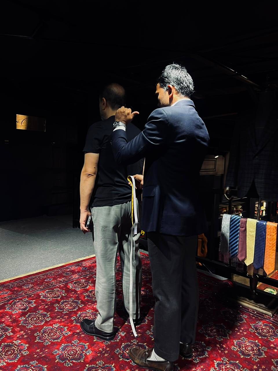 Tailor checking jacket hem and back balance on a client