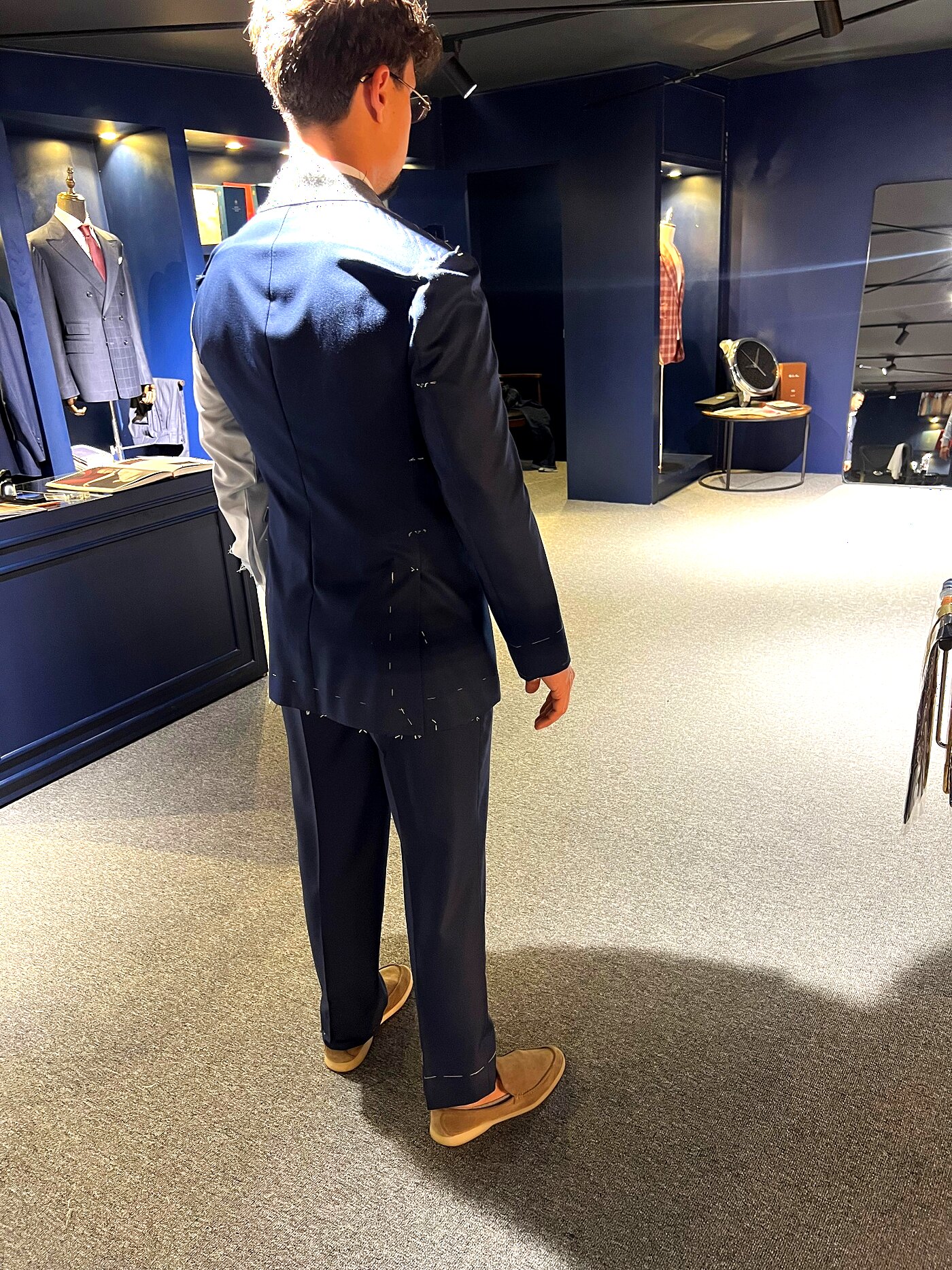 Back view of a client in a basted navy two-piece suit in the showroom