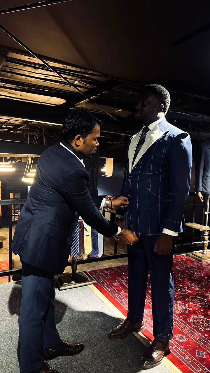 Tailor adjusting the front of a navy chalk-stripe suit on a tall client