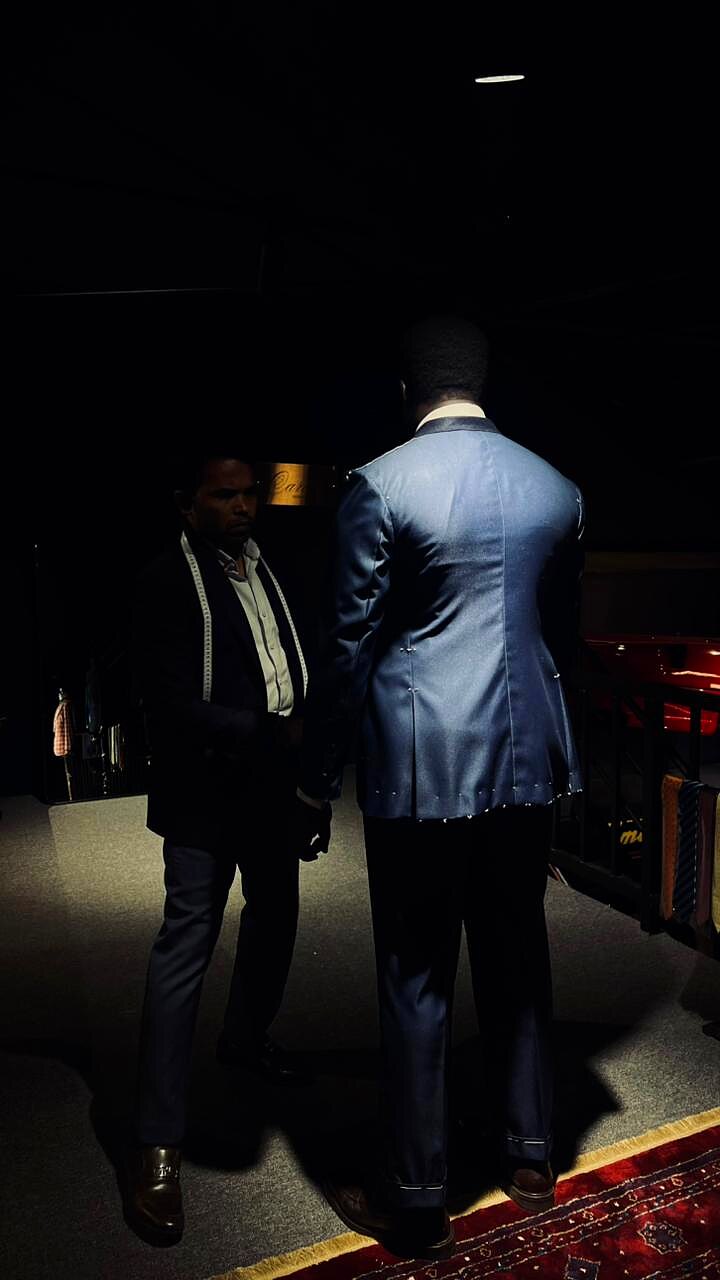 Cutter inspecting a navy jacket on a client under low atelier light