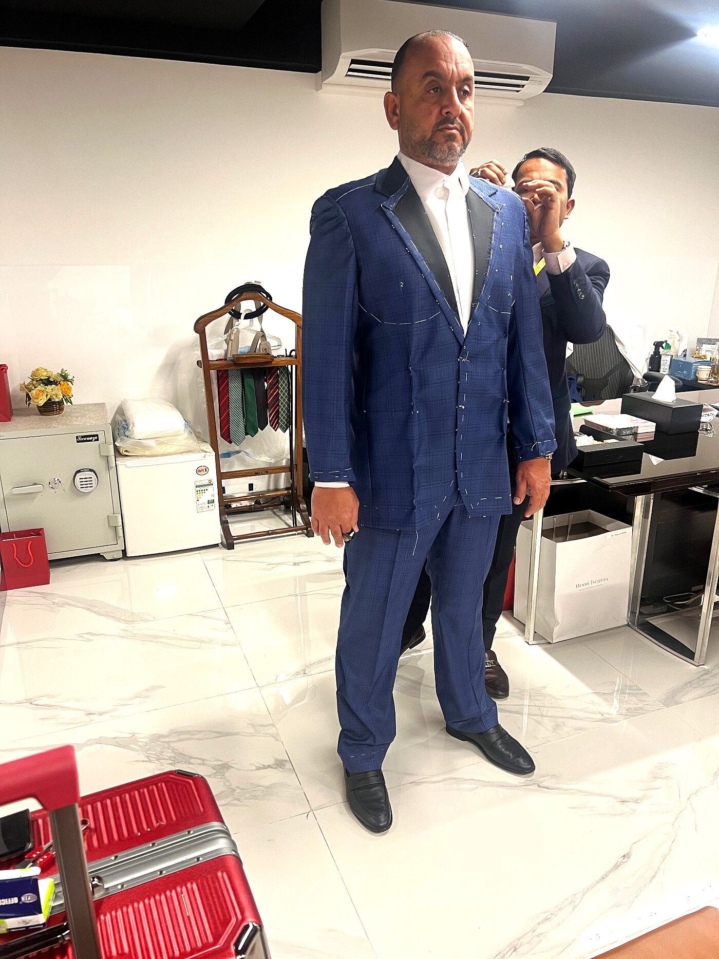 Tailor pinning shoulder of a blue check basted jacket on a standing client
