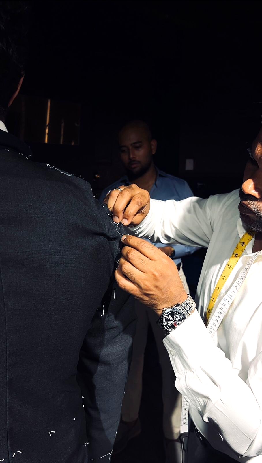 Close-up of a tailor's hands pinning the lapel of a grey jacket