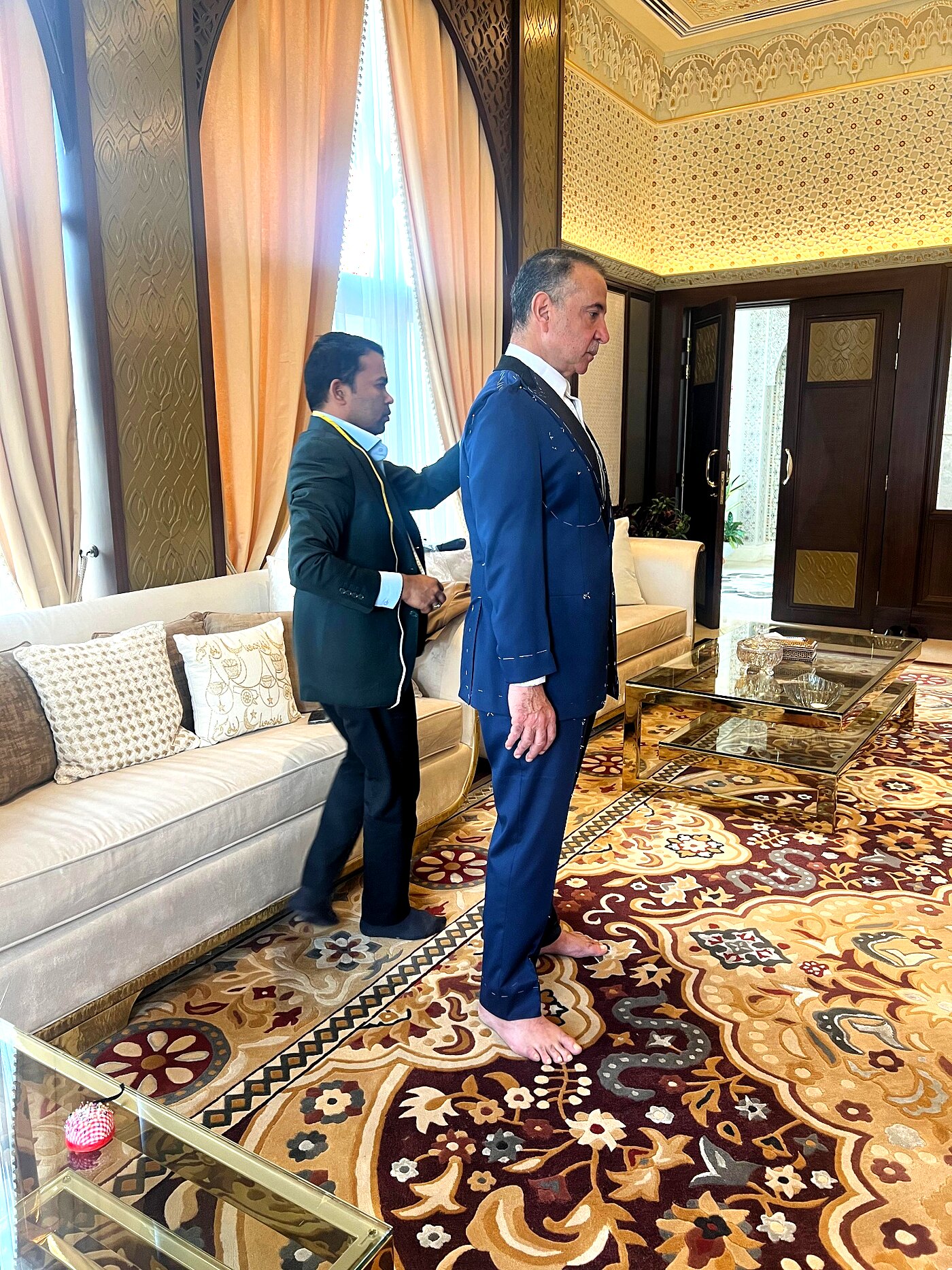 Private fitting at a client's suite — tailor pinning a navy jacket
