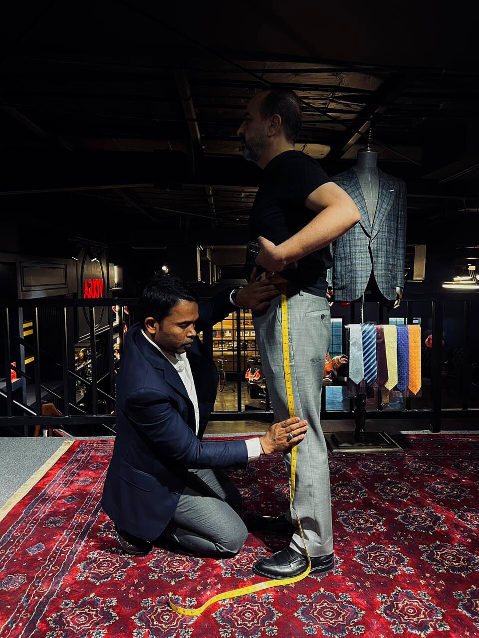 Tailor kneeling to measure trouser outseam of a standing client